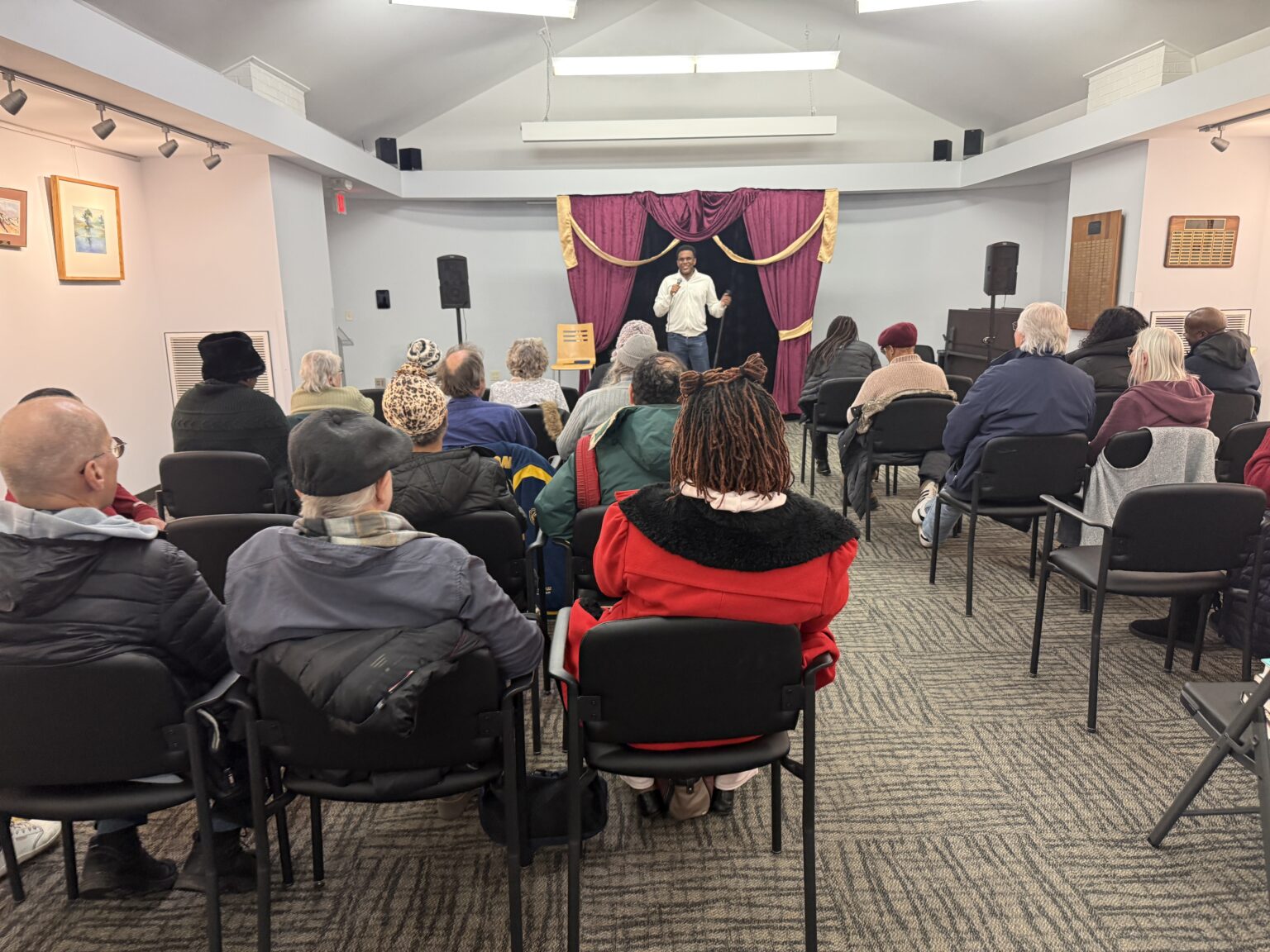 A Laugh at the Library comedy show in progress in a library meeting room, with a full audience of adults watching a comedian on stage